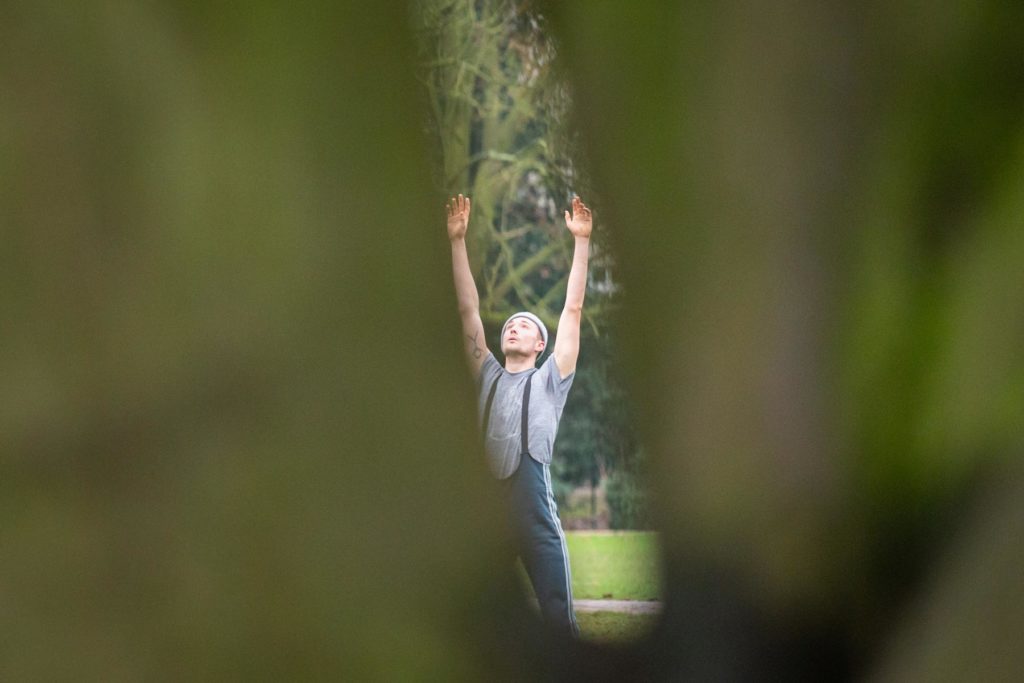 Joshua Alsen ist zwischen einer Baumspalte zu erkennen, während er seine Arme in die Lüfte streckt und in den Himmel schaut.
