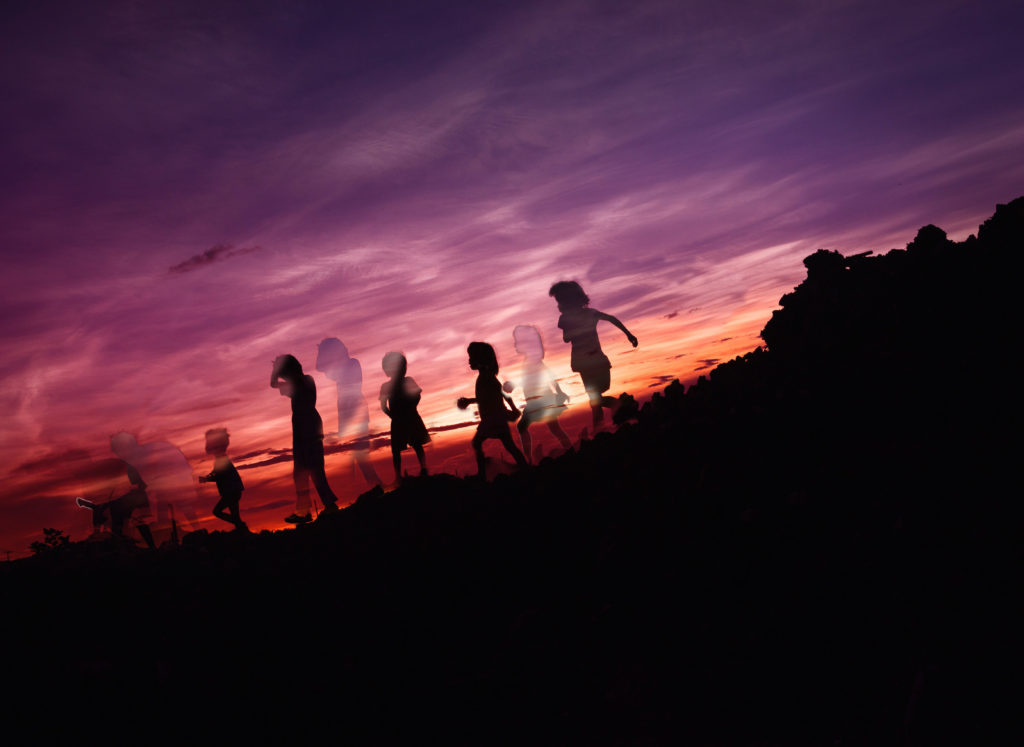 Das Foto zeigt einen lila orangen Sonnenuntergang, vor dem die Silhouetten von sechs Kindern zu sehen sind. Durch die Bearbeitung sind manche von ihnen jedoch als Schatten doppelt zu sehen. Dies dient dazu, die Frage nach dem Kinderwunsch visuell darzustellen.